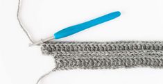 the crochet stitch is being worked on with a blue handled knitting needle in front of it