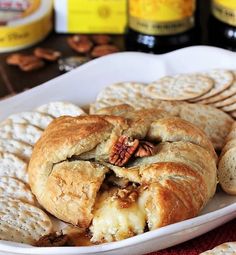 a white plate topped with crackers covered in cheese and nuts next to wine bottles