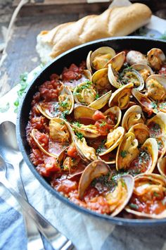 a pan filled with pasta and clams on top of a table next to bread