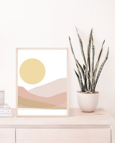 a plant is sitting on top of a dresser next to a framed art print that says desert sunset