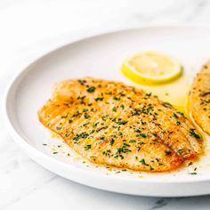 two fish fillets on a white plate with lemon wedges