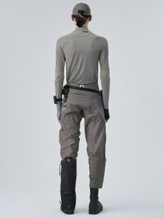 the back view of a person in grey pants and black boots, standing on a white background