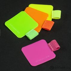 three pieces of neon colored luggage on a black surface, one has a pink ribbon and the other is green