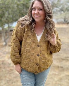 a woman standing in the grass wearing a brown cardigan sweater and jeans with her hand on her hip