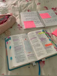 an open book sitting on top of a bed next to a pink bag and pen