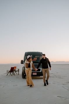 two people holding hands in front of a truck on the beach with chairs around them