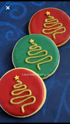 three decorated cookies with christmas trees on them sitting on a blue tablecloth covered surface