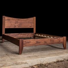 a wooden bed frame sitting on top of a cement floor next to a black wall