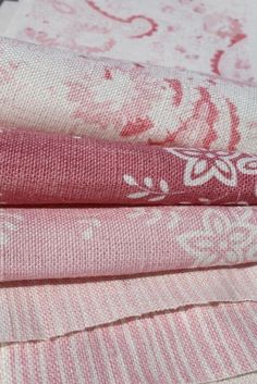 pink and white fabrics stacked on top of each other in different patterns, sizes and colors