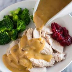 someone pouring gravy on chicken with broccoli and cranberry sauce