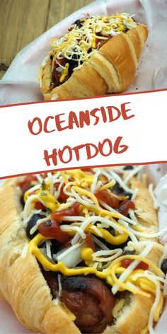 two hotdogs with cheese and other toppings on them, next to a sign that says oceanside hotdog