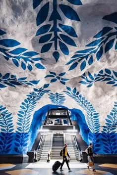 two people are walking down an escalator with blue leaves painted on the ceiling