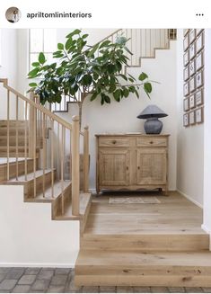 a living room with stairs and a potted plant on the sideboard in front of it