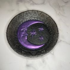 a purple moon and stars in a black bowl on a marble counter top with white background