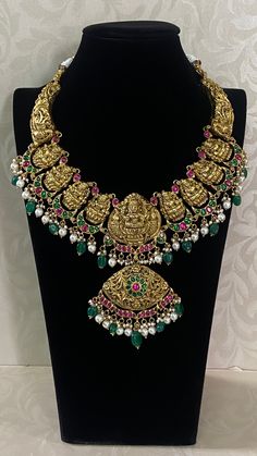 The Antique Kundan Lakshmi Necklace is a masterpiece of traditional Indian craftsmanship, representing the regal heritage of temple jewelry. At its centerpiece, it features a finely detailed depiction of Goddess Lakshmi, the Hindu goddess of wealth and prosperity, intricately carved in gold. Surrounding the central deity are vibrant, hand-set Kundan gemstones—emeralds, rubies, and diamonds��—arranged in floral and geometric patterns. The necklace is designed with each element embossed with antique Luxury Meenakari Temple Necklace For Diwali, Temple Necklace, Goddess Of Wealth, Hindu Goddess, Temple Jewelry, Wealth And Prosperity, Indian Necklace, The Hindu, Golden Jewelry