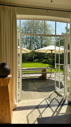 an open glass door leading to a patio with tables and umbrellas in the background