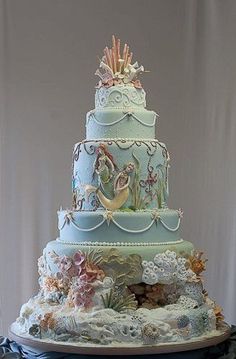 a three tiered blue cake with sea creatures on the sides and under it is sitting on a table