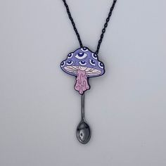 a blue and pink mushroom necklace with a spoon hanging from it's side on a black chain