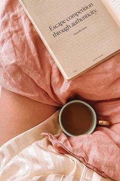 a cup of coffee sitting on top of a pink blanket next to an open book