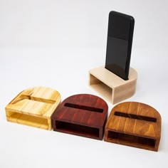 three wooden cell phones stand next to each other in front of a phone holder on a white background