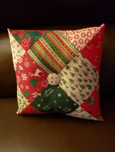 a red and green patchwork pillow sitting on top of a brown couch