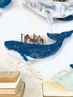 three blue whale sculptures are hanging on the wall next to books and teapots