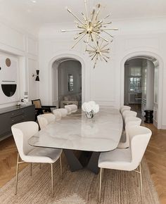 a dining room table with white chairs and a chandelier