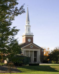 an old church with a clock tower and steeple on the top is surrounded by green grass