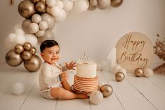 a baby sitting on the floor with a cake in front of him and some balloons