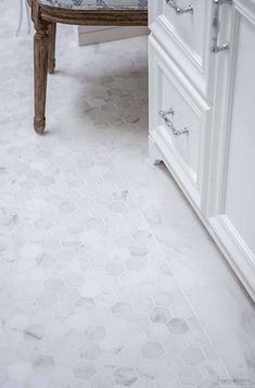 a white bathroom with hexagonal tiles on the floor and countertop, along with a wooden chair