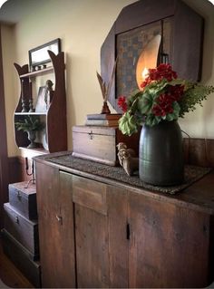 a vase filled with red flowers sitting on top of a wooden dresser next to a mirror