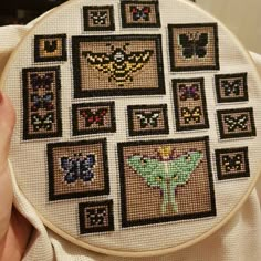 a person holding up a cross stitched butterfly pattern on a white piece of cloth