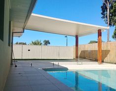 an empty swimming pool next to a white fenced in area with trees and bushes