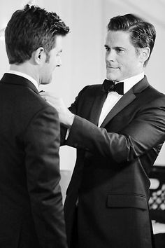 two men in tuxedos standing next to each other with their hands on the chest