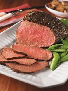 a white plate topped with meat and green beans on top of a wooden table next to other foods