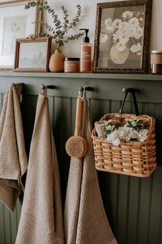 towels hanging on the wall next to a basket with flowers in it and pictures above