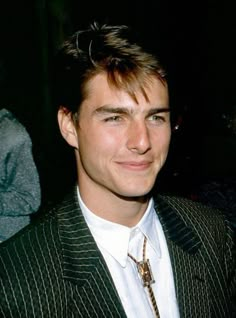 a man in a pinstripe suit smiling for the camera with his hair pulled back