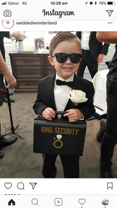 a little boy dressed in a tuxedo holding a ring security box