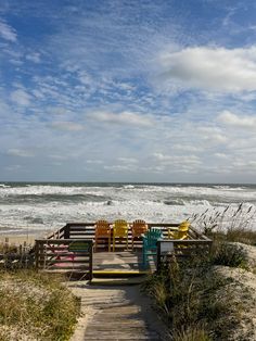 two colorful chairs sitting on top of a wooden walkway next to the ocean and beach