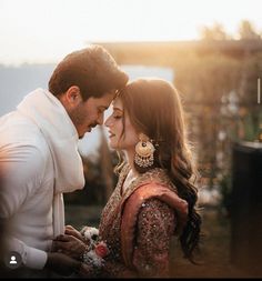 a man and woman standing next to each other in front of a building with the sun behind them