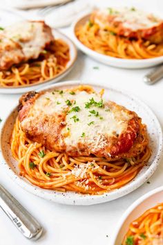 several plates of spaghetti with meat and parmesan cheese on the top one plate has chicken parmesan