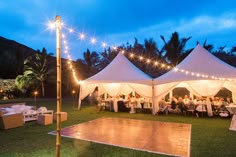 a dance floor is set up in the middle of a lawn with white tents and string lights