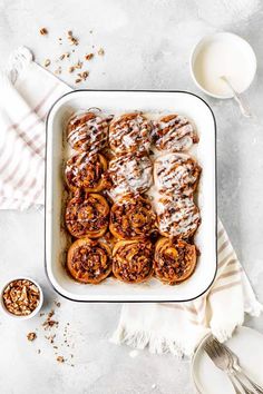 cinnamon rolls in a baking dish with icing drizzled on top and spoons next to it