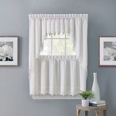 a window with white curtains and flowers on the windowsill in front of two framed pictures