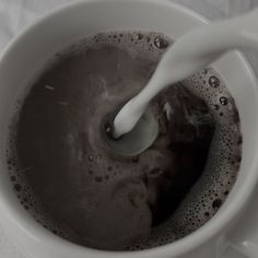 milk being poured into a coffee cup filled with brown liquid on top of a white table cloth