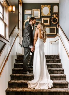 a bride and groom are standing on the stairs in their wedding attire, looking at each other