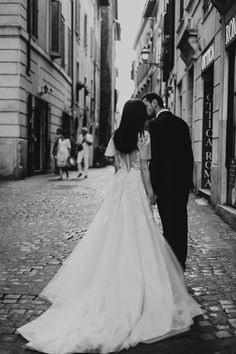 a bride and groom walking down the street in an old european city, holding hands