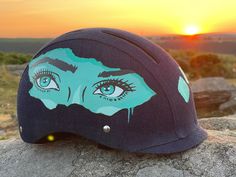 a helmet with an image of a woman's face painted on it sitting on top of a rock