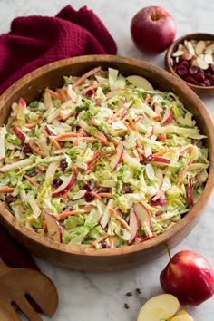 a wooden bowl filled with coleslaw next to an apple and cranberry salad