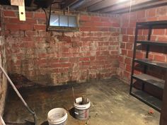 two buckets are sitting on the floor in an unfinished room with red brick walls